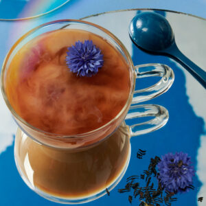 Clear cup of black tea with a splash of milk against a blue background.