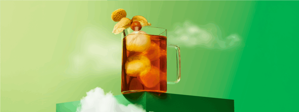 A clear glass filled with richly-coloured iced tea with a ground cherry on the rim, set against a green backdrop with clouds.